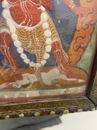 A Tibetan thangka in inlaid gilt brass frame, 19th C.